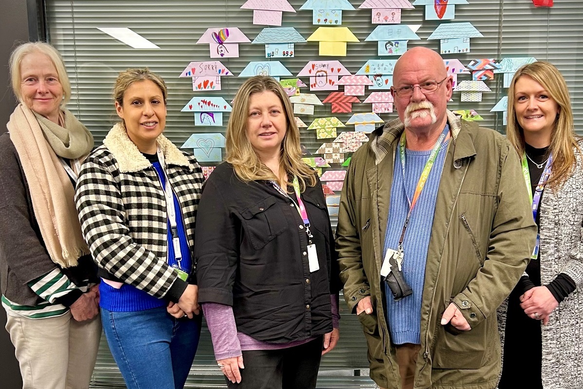 Five AccessCare team members stand in front of a wall decorated with origami houses.